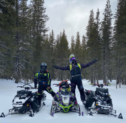 Two people pose with three snowmobiles