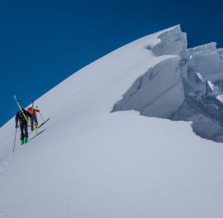 Backcountry skiers hiking near a large cornice.